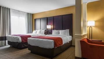 Quarto de hotel com duas camas, uma escrivaninha, uma cadeira e um abajur.