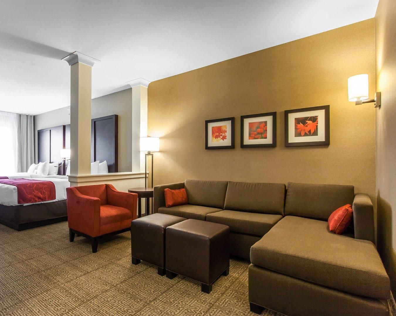 A hotel room with a bed, a sofa, two armchairs, a coffee table, and a wall with three framed pictures.