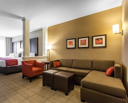 Habitación de hotel con cama, sofá, dos sillones, una mesa de centro y una pared con tres cuadros enmarcados.