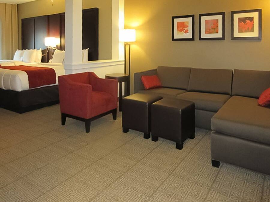 Une chambre d’hôtel avec un lit, un fauteuil rouge, un canapé gris et une petite table. Trois tableaux encadrés sont accrochés au mur.