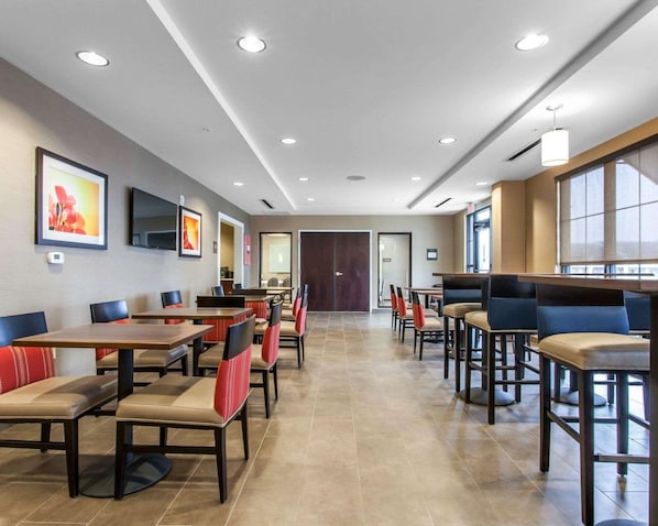 Un'area ristorazione di un hotel con diversi tavoli e sedie, una televisione a schermo piatto montata sulla parete e un'ampia finestra che offre luce naturale.