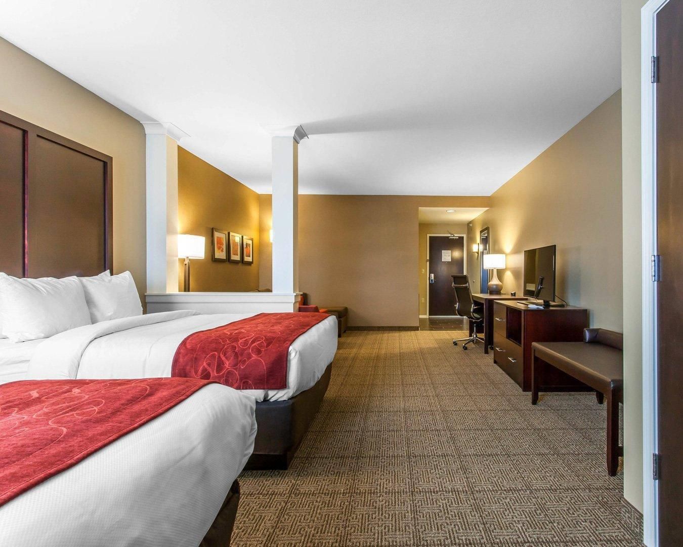 A hotel room with two beds, a desk, a chair, a mirror, and a carpeted floor.
