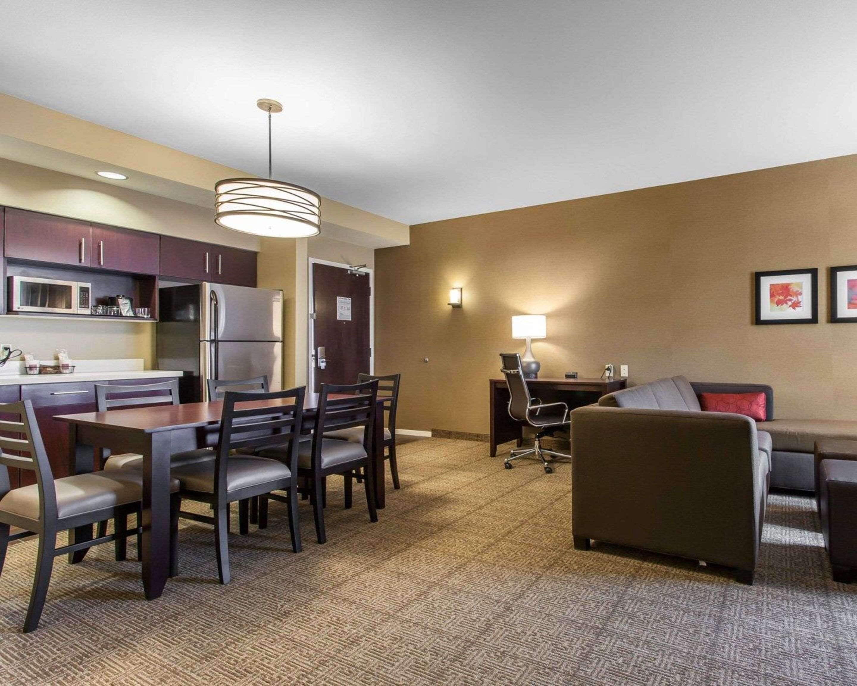 A hotel room with a kitchenette, dining area, and a living area with a sofa and a desk.