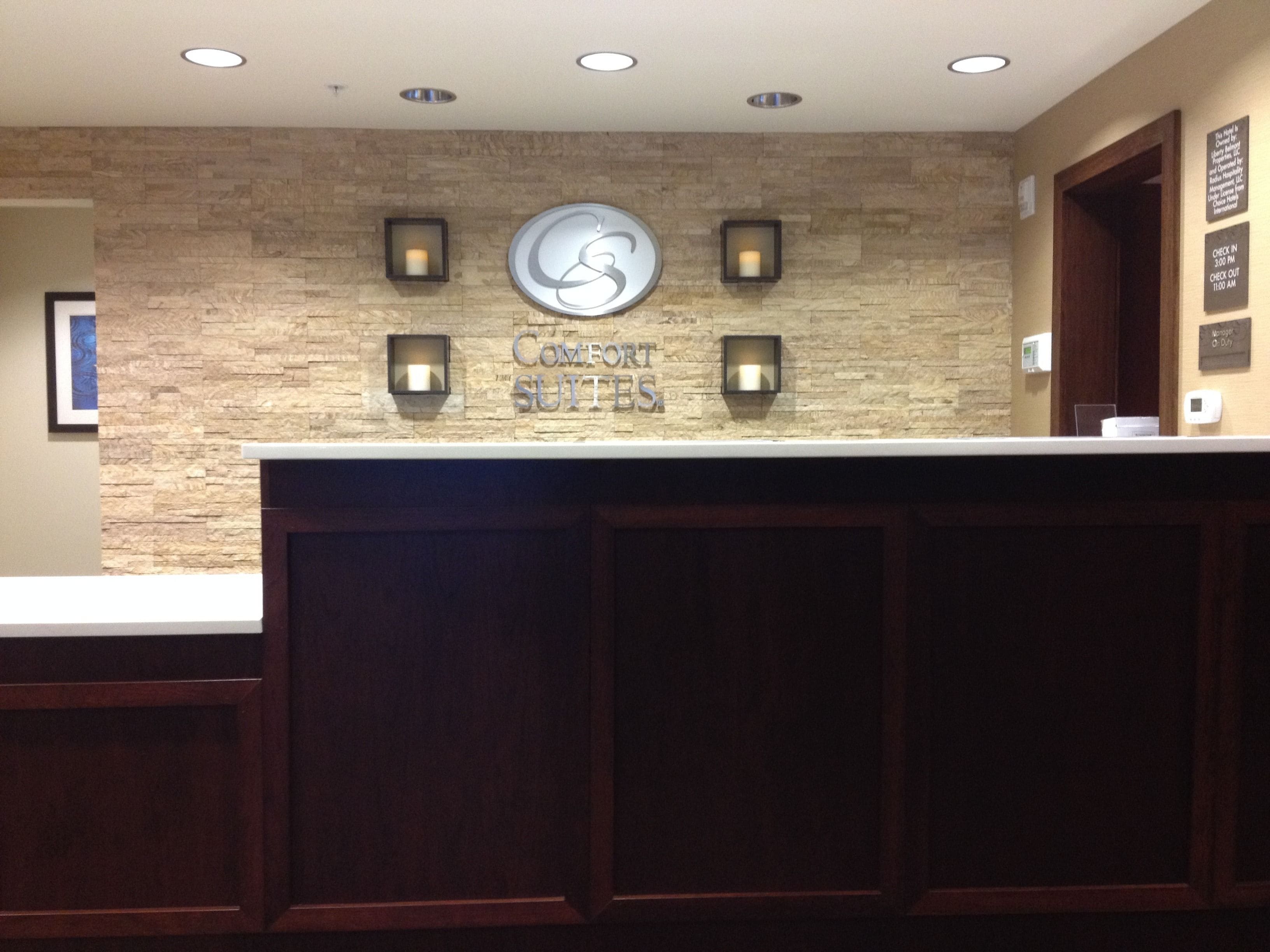 A reception desk with a stone wall backdrop, a large illuminated 'S' logo, and a 'COMFORT SUITES' sign.