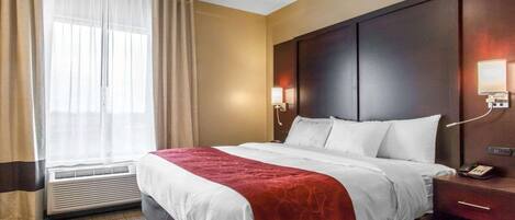 A hotel room with a large bed, a bedside table with a phone, a wall-mounted light, and a window with curtains.