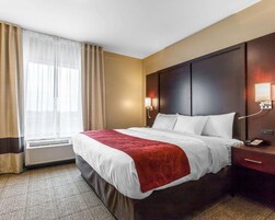 Habitación de hotel con una cama grande, una mesita de noche con teléfono, una lámpara de pared y una ventana con cortinas.