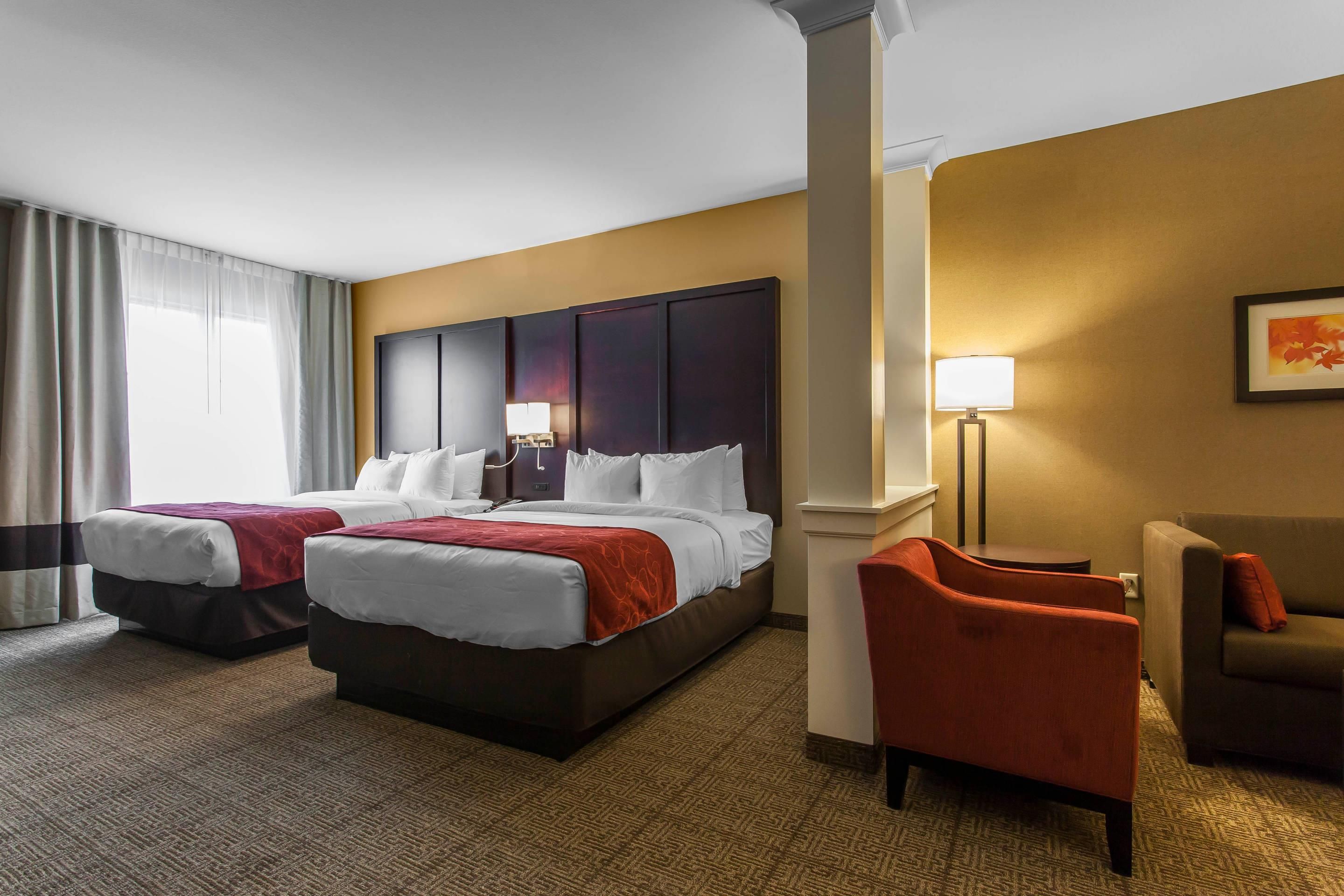 Une chambre d’hôtel avec deux lits, un bureau, une chaise et une lampe.