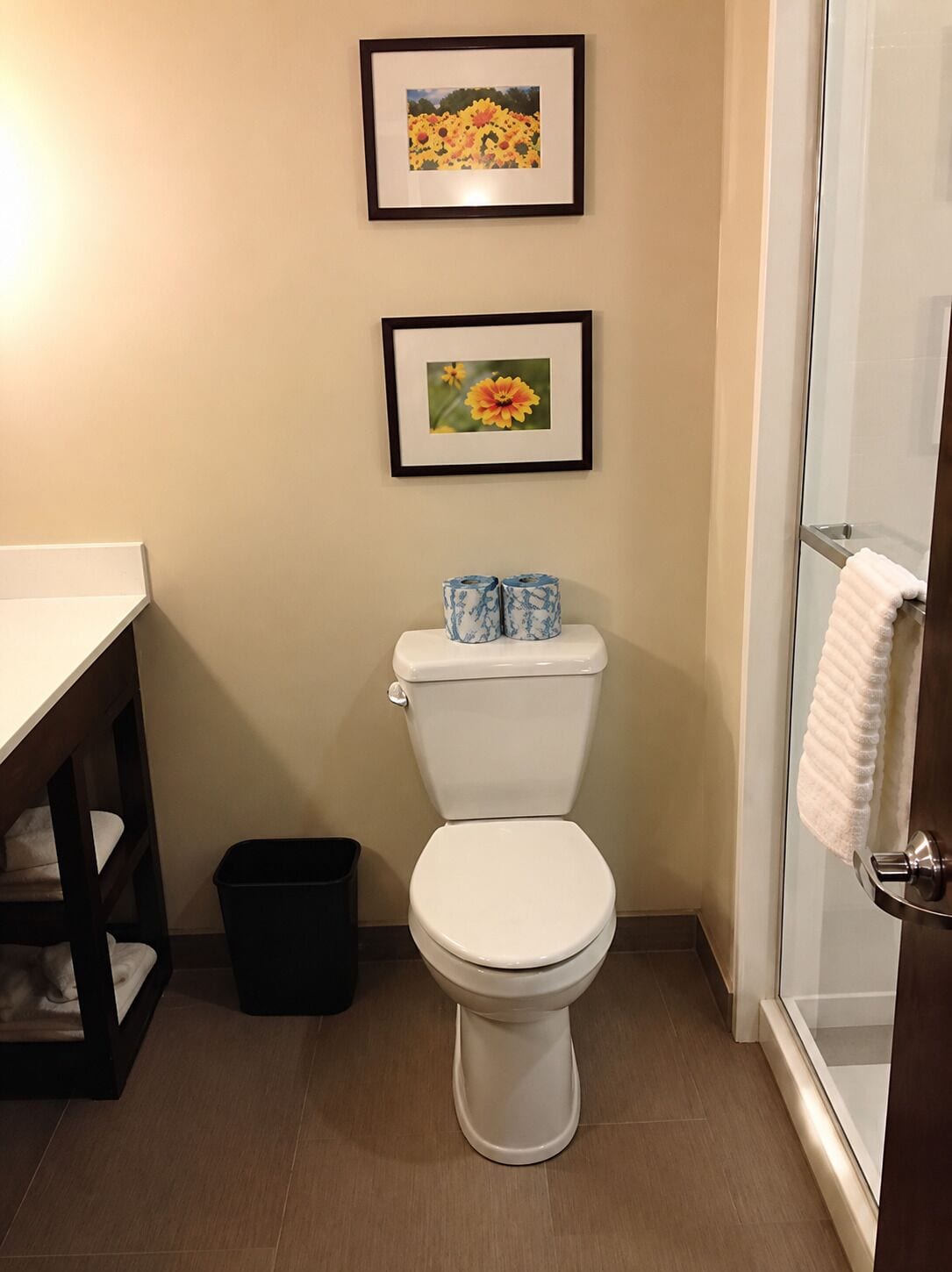 Ein Badezimmer mit Toilette, blumigen Bildern an der Wand, einer Duschkabine und einem Mülleimer.