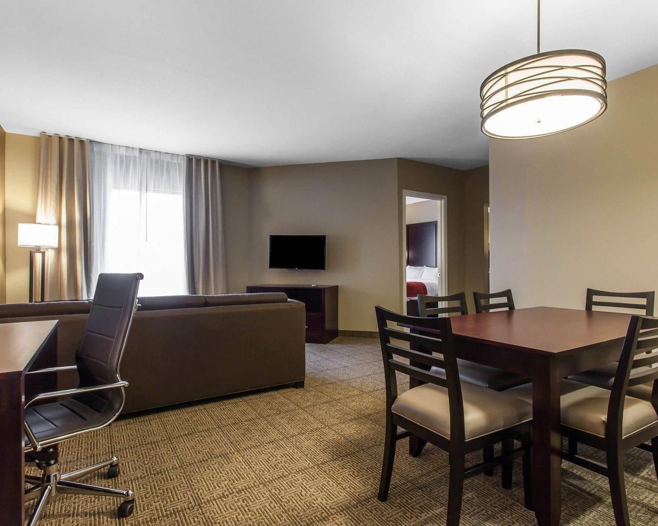A hotel room with a sofa, a dining table with chairs, a TV, and a lamp.