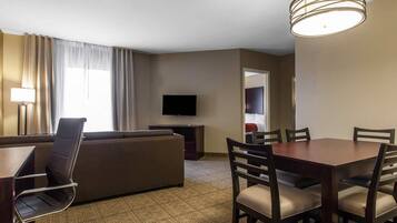 A hotel room with a sofa, a dining table with chairs, a TV, and a lamp.