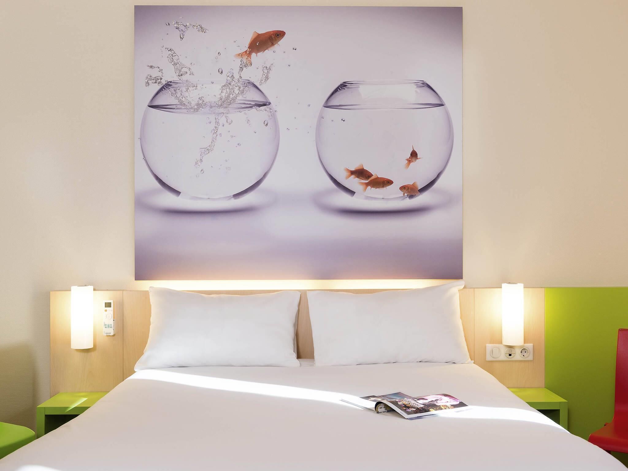 Een hotelkamer met een bed, twee nachtkastjes, een wandlamp en een poster met vissen in water.