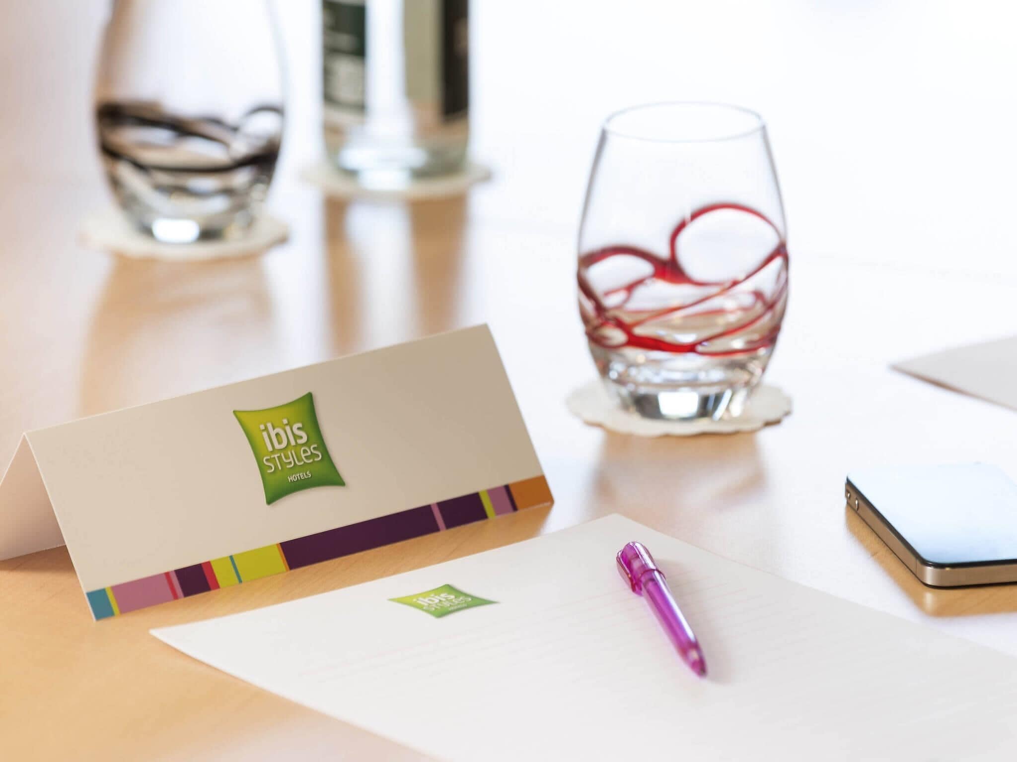 A hotel business card, a pen, and a glass with a red design on a table.