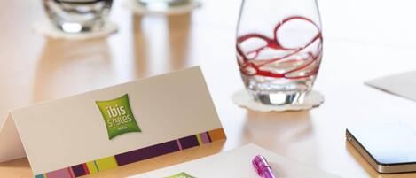 A hotel business card, a pen, and a glass with a red design on a table.