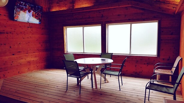 A wooden cabin with a round table and four chairs, large windows, and a television mounted on the wall. - Americas Best Value Inn & Suites Atlantic (Atlantic)