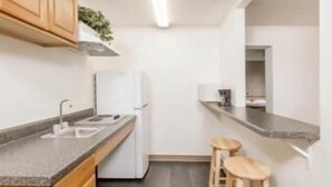 A modern kitchen with wooden cabinets, a white refrigerator, a sink, and two stools. - Americas Best Value Inn & Suites Atlantic (Atlantic)