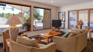 A living room with beige sofas, a wooden coffee table, a television on a stand, and a large window with blinds. - Americas Best Value Inn & Suites Atlantic (Atlantic)