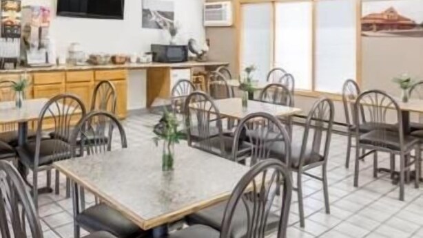 A dining area with multiple tables and chairs, a kitchen area with cabinets and appliances, and a television mounted on the wall.