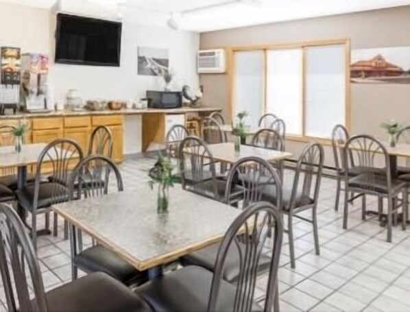 A dining area with multiple tables and chairs, a kitchen area with cabinets and appliances, and a television mounted on the wall.