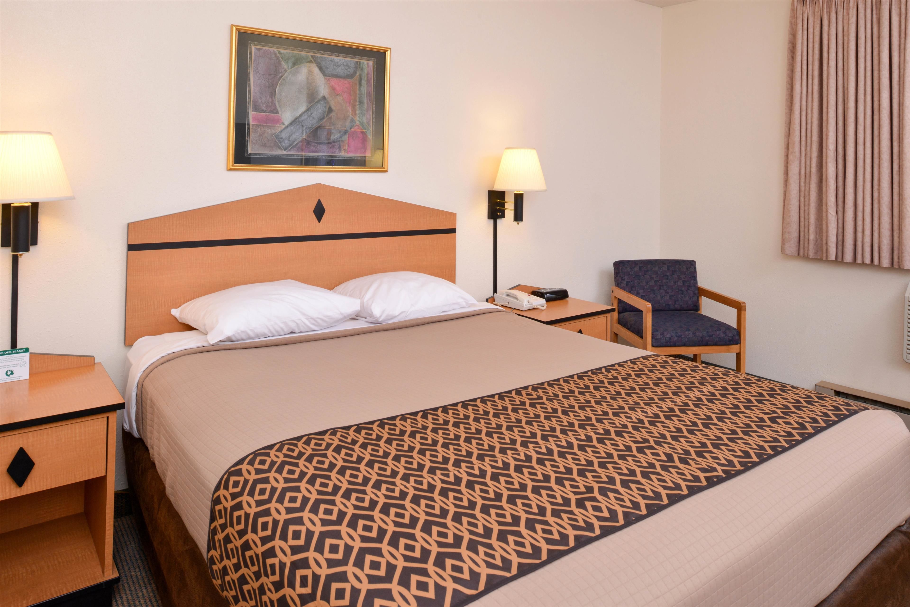 Een hotelkamer met een bed, twee nachtkastjes, een stoel, een lamp en een schilderij aan de muur.