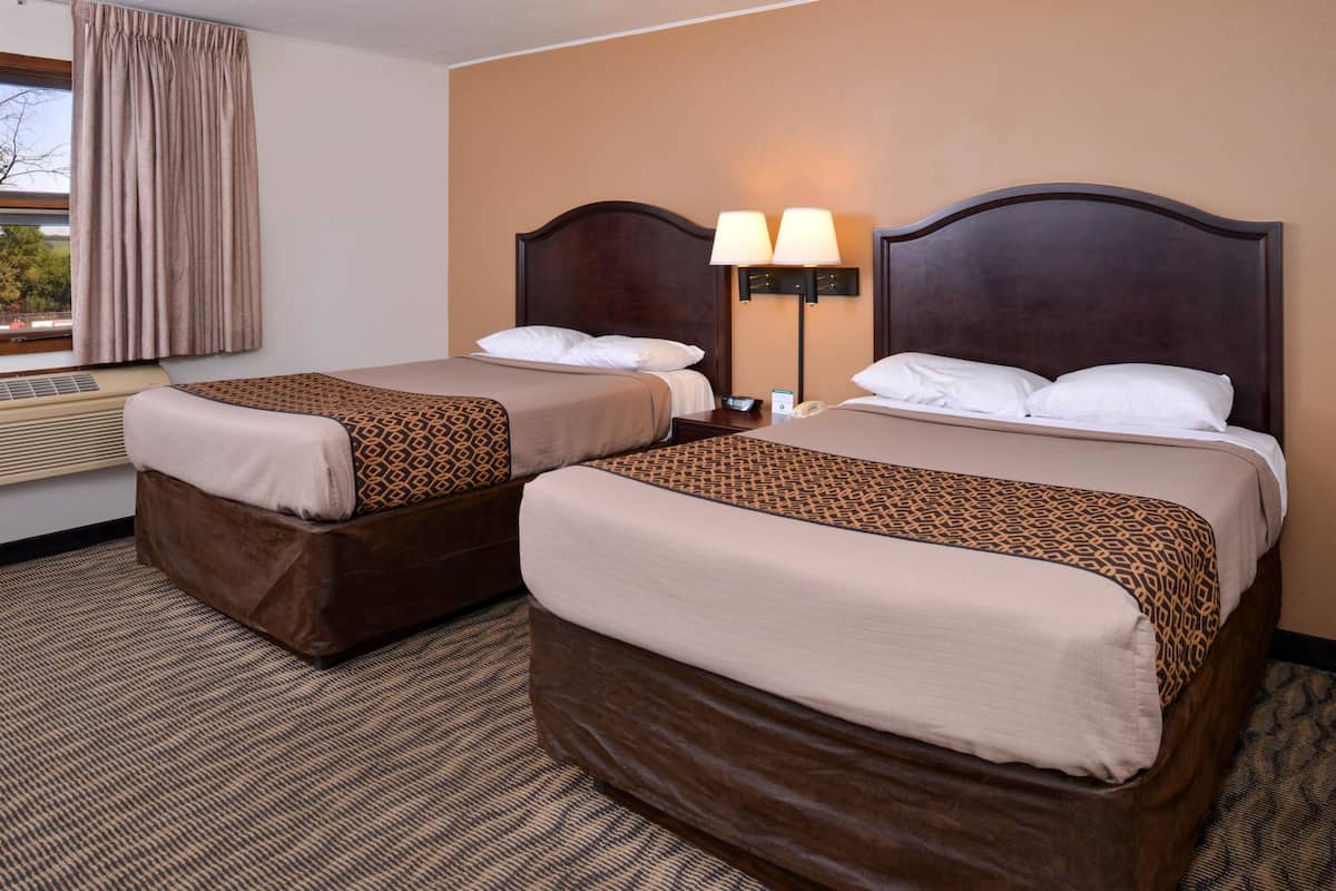 Quarto de hotel com duas camas, janela com cortinas, ar-condicionado e mesa de cabeceira com abajur.