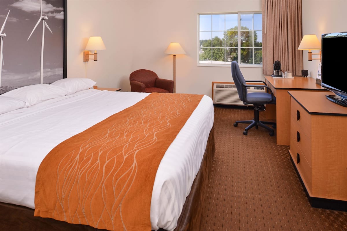 Quarto de hotel com cama, escrivaninha, cadeira e televisão.