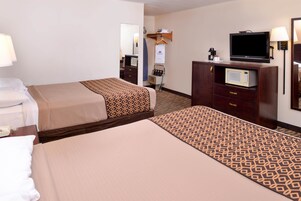 Habitación de hotel con dos camas, televisión, microondas y escritorio con lámpara.