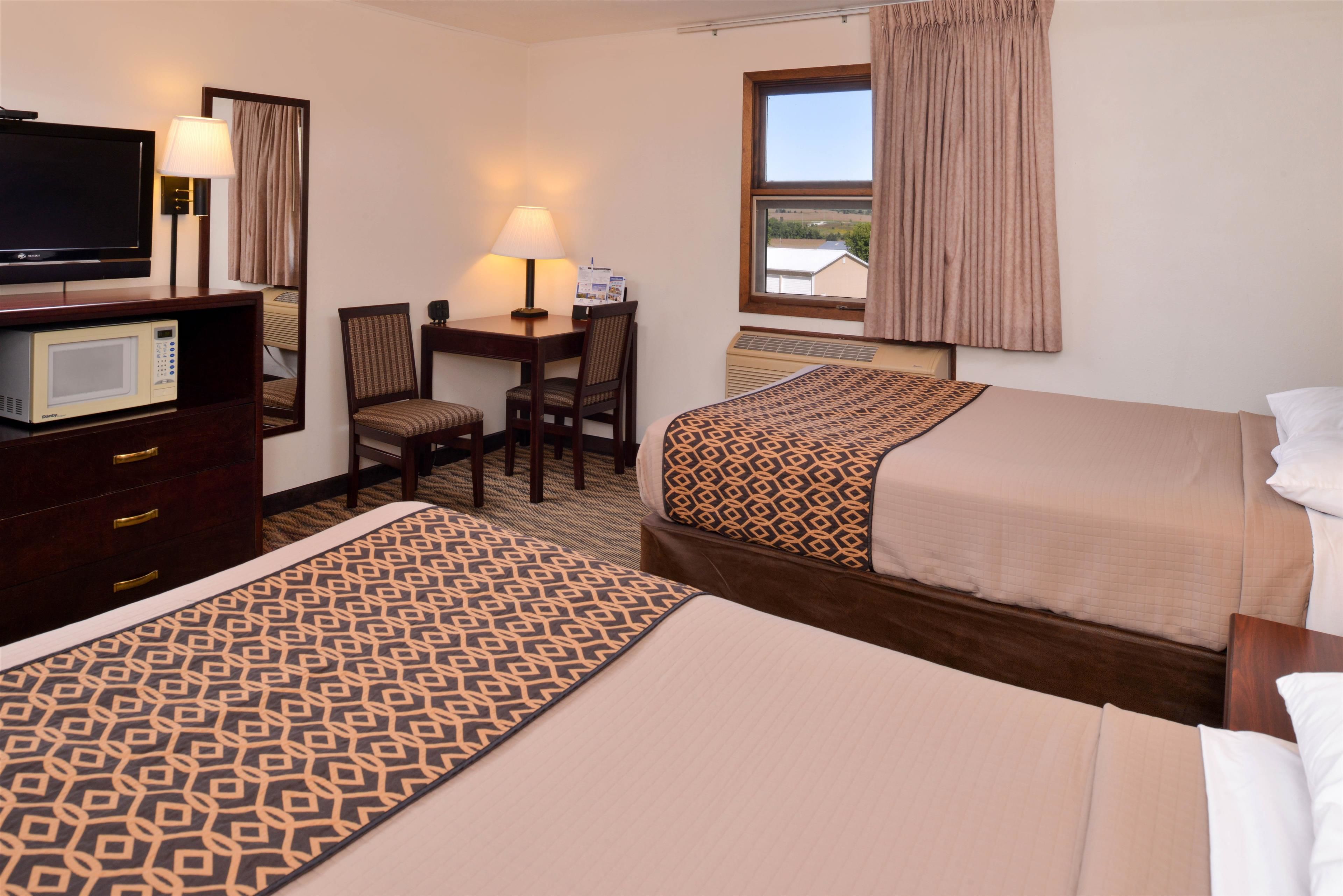 A hotel room with two beds, a desk with a chair, a television, a microwave, and a window with curtains.