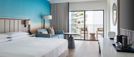 A hotel room with a large bed, a sofa, a small table, and a balcony with a view of the building.