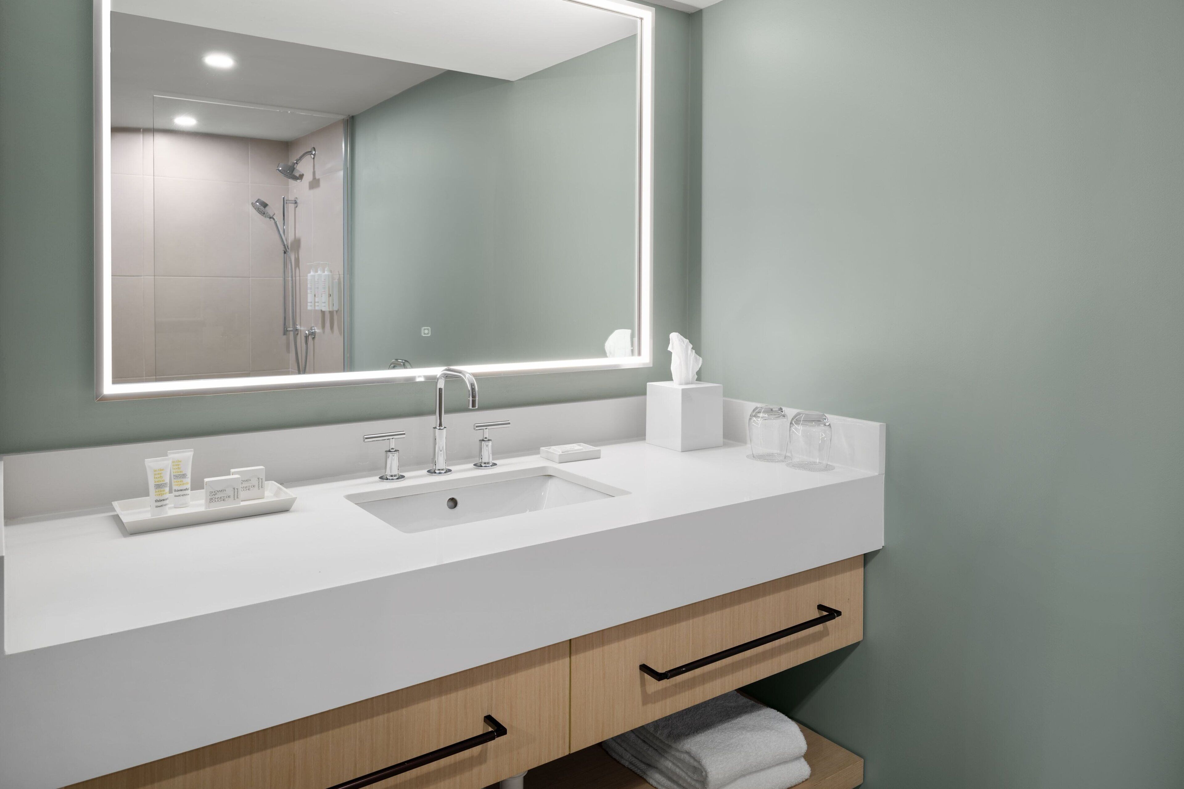 Un baño moderno con un espejo grande, lavamanos blanco y armarios de madera.