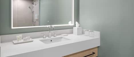Un baño moderno con un espejo grande, lavamanos blanco y armarios de madera.