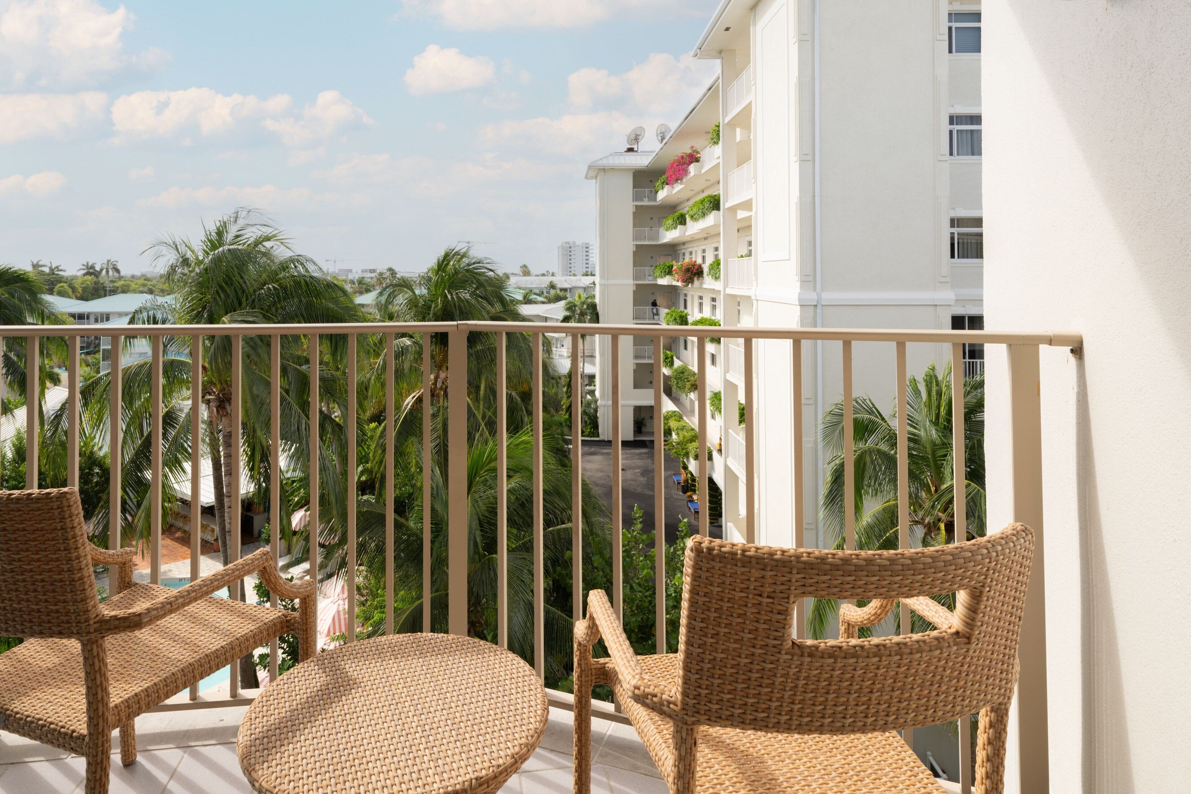 Ein Balkon mit Korbmöbeln und Blick auf ein Gebäude mit Balkonen und Pflanzen.