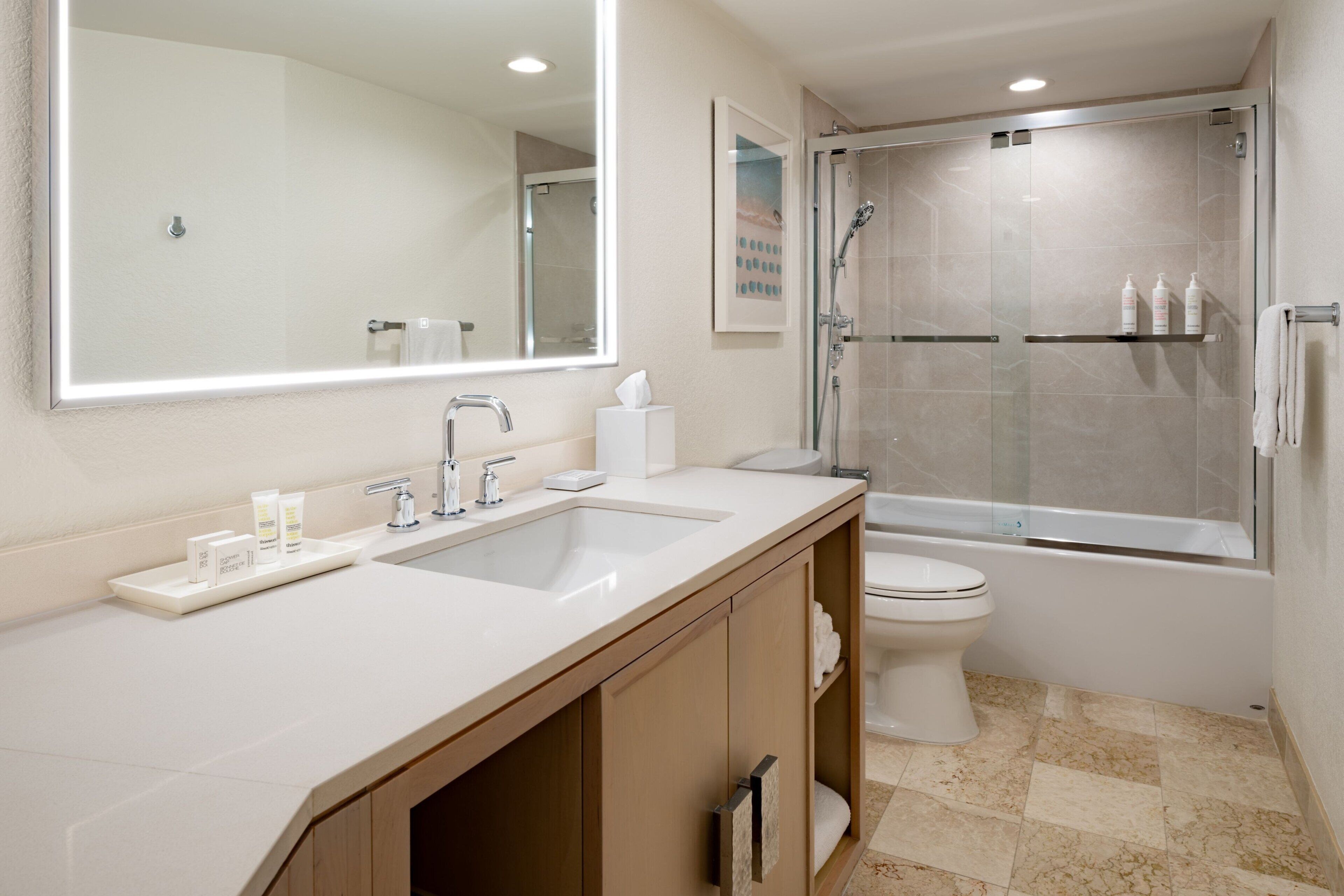 Une salle de bain moderne dotée d’un grand miroir, de deux lavabos, de toilettes et d’une douche à parois de verre.