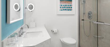 A modern bathroom with a white sink, two round mirrors, a toilet, and a glass-enclosed shower.