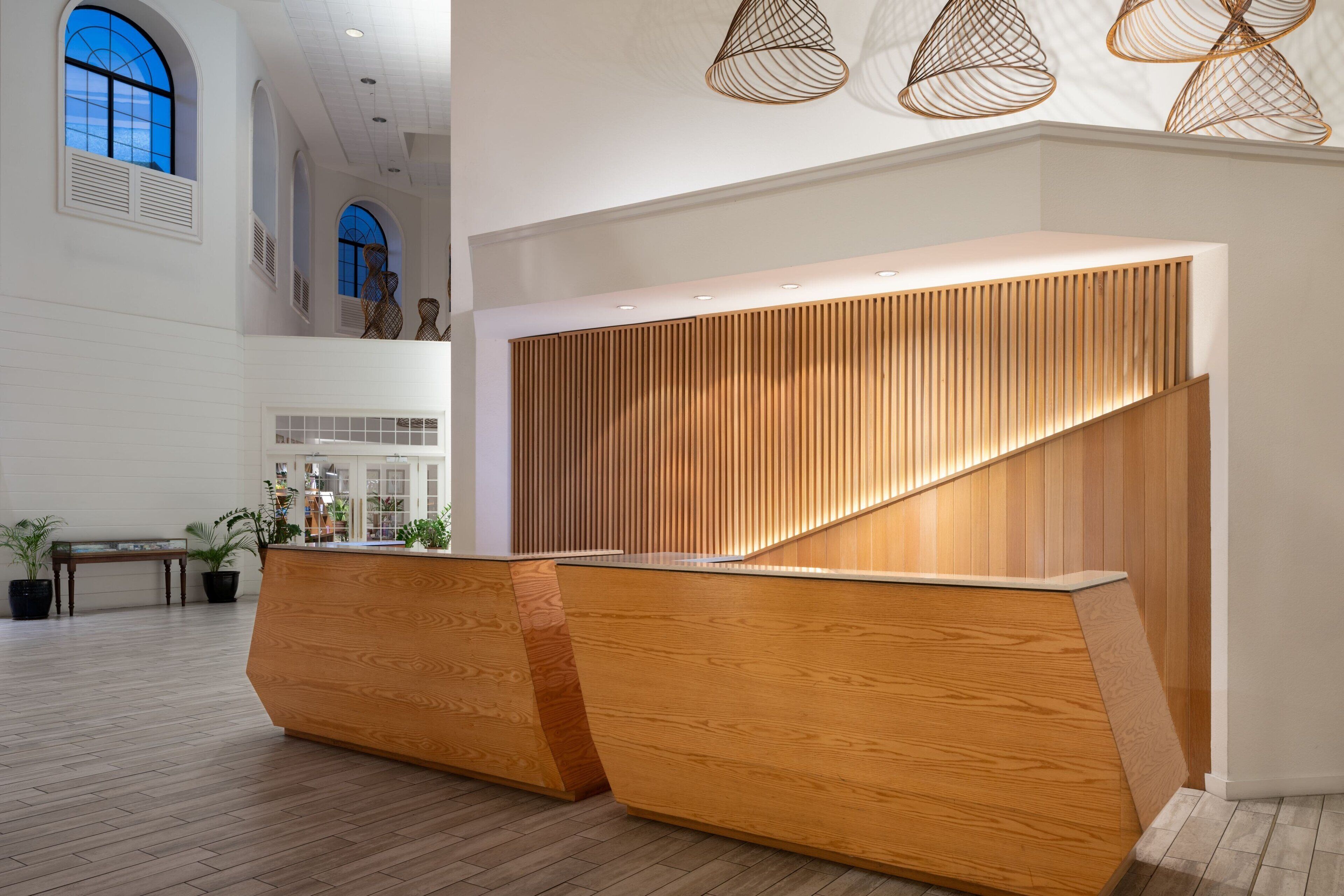 A reception area with a wooden reception desk, potted plants, and a high ceiling with arched windows.