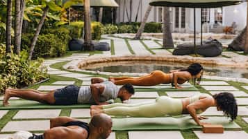 A group of people doing yoga on mats in an outdoor setting with a garden and a water feature.