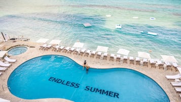 Relax by the ENDLESS SUMMER pool surrounded by sun loungers and umbrellas, with access to a sandy beach.