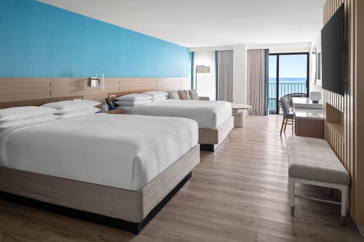 A hotel room with two beds, a desk, a chair, and a TV.
