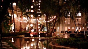 A nighttime view of a hotel courtyard with a pool, palm trees, and string lights. - Grand Cayman Marriott Beach Resort (Seven Mile Beach)