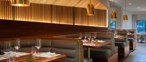 A modern restaurant with wooden paneling, green cushioned booths, and pendant lighting.