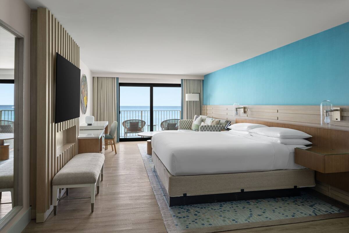 A modern hotel room with a large bed, a desk, a chair, and a view of the ocean.