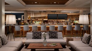 A modern bar area with a bar counter, stools, and a television screen. - Grand Cayman Marriott Resort (Seven Mile Beach)