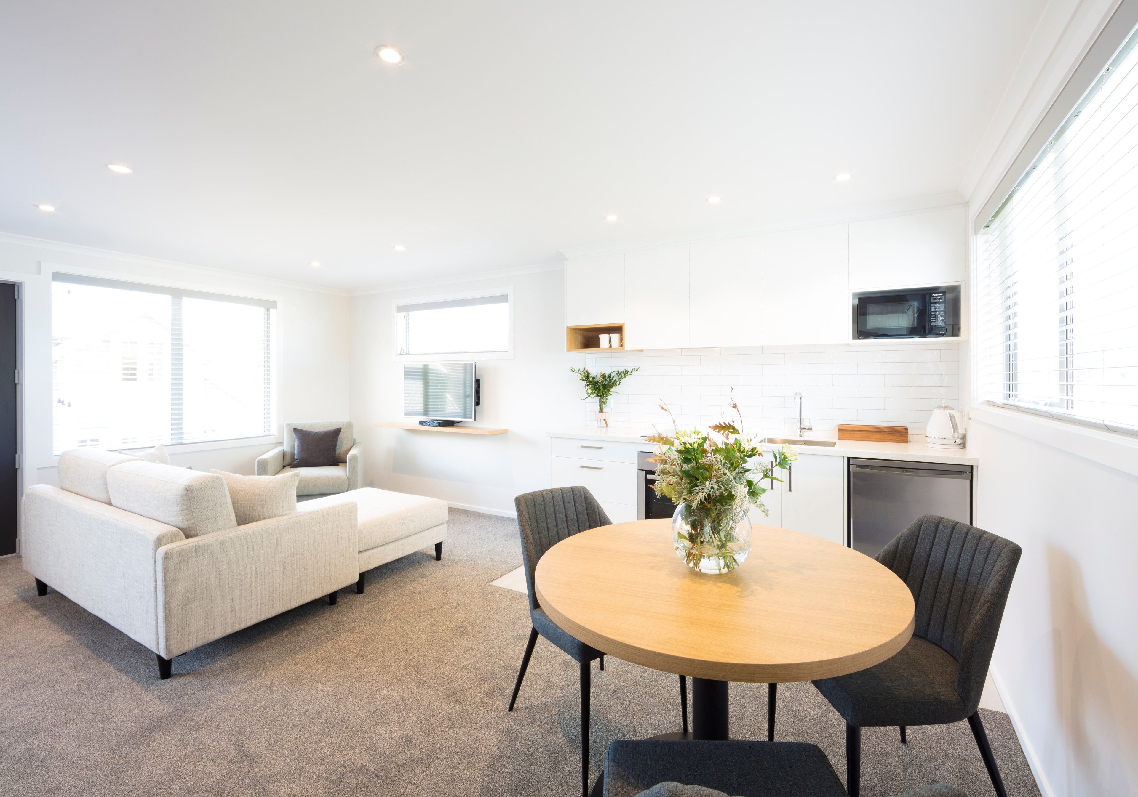 A modern living room with a sofa, a dining table with chairs, and a kitchen area with a microwave and sink.