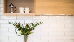 A kitchen with white tiles, a wooden cabinet, a coffee maker, two white cups, and a vase with flowers. - Beechwood Boutique Accommodation (Dunedin)