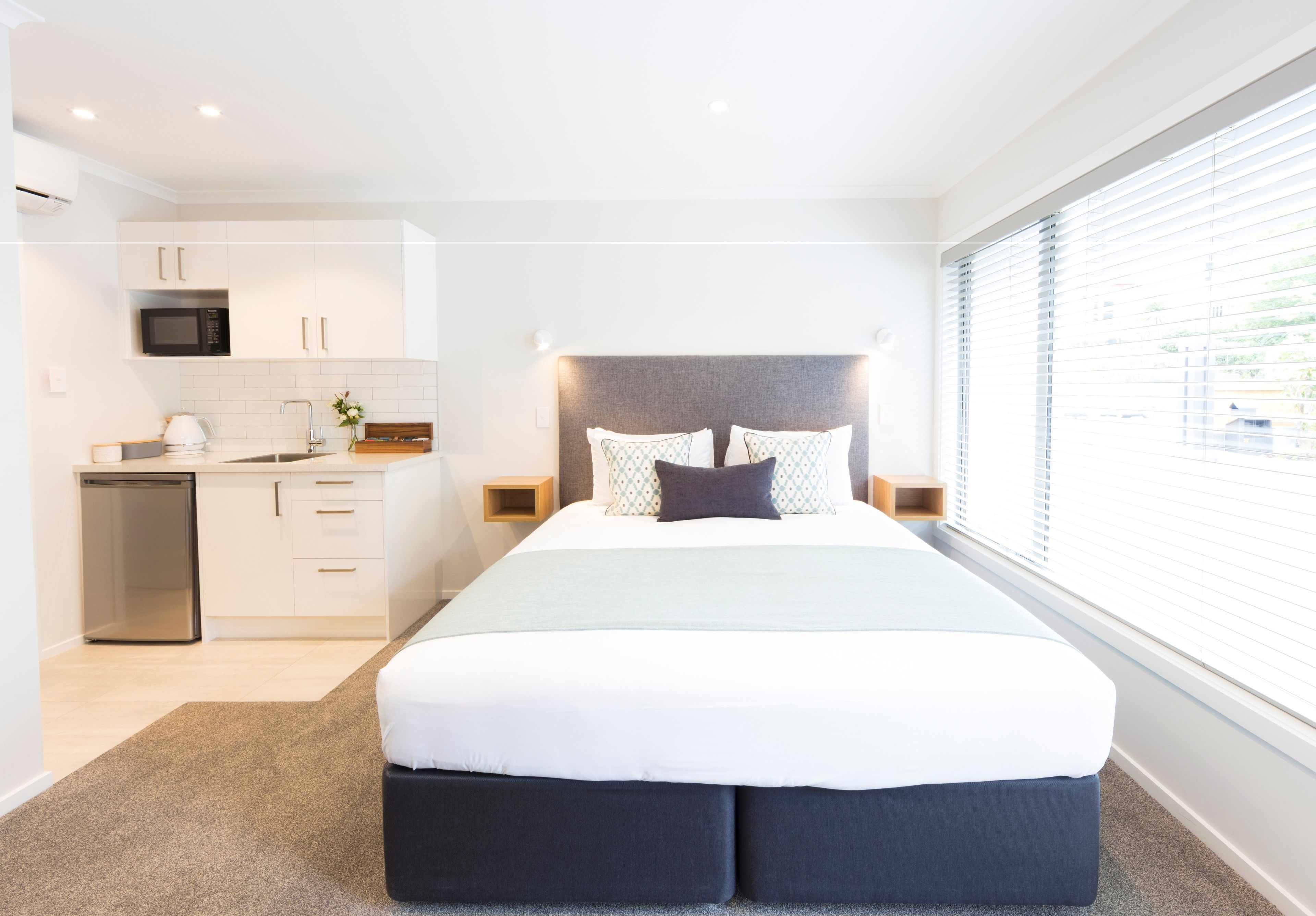 A modern bedroom with a large bed, a built-in microwave, and a compact kitchenette.