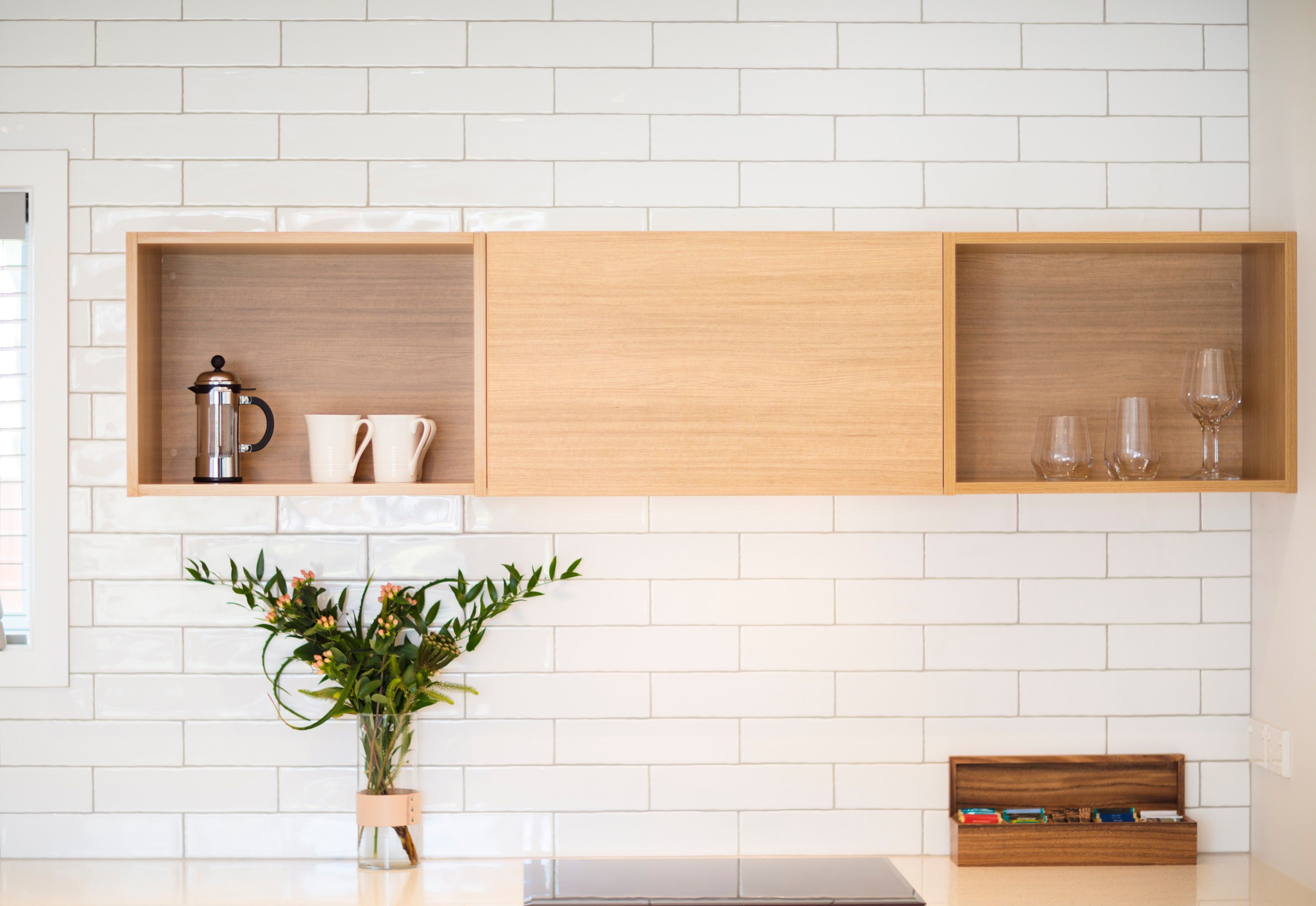 A kitchen with white tiled backsplash, wooden shelves with kitchenware, and a potted plant.