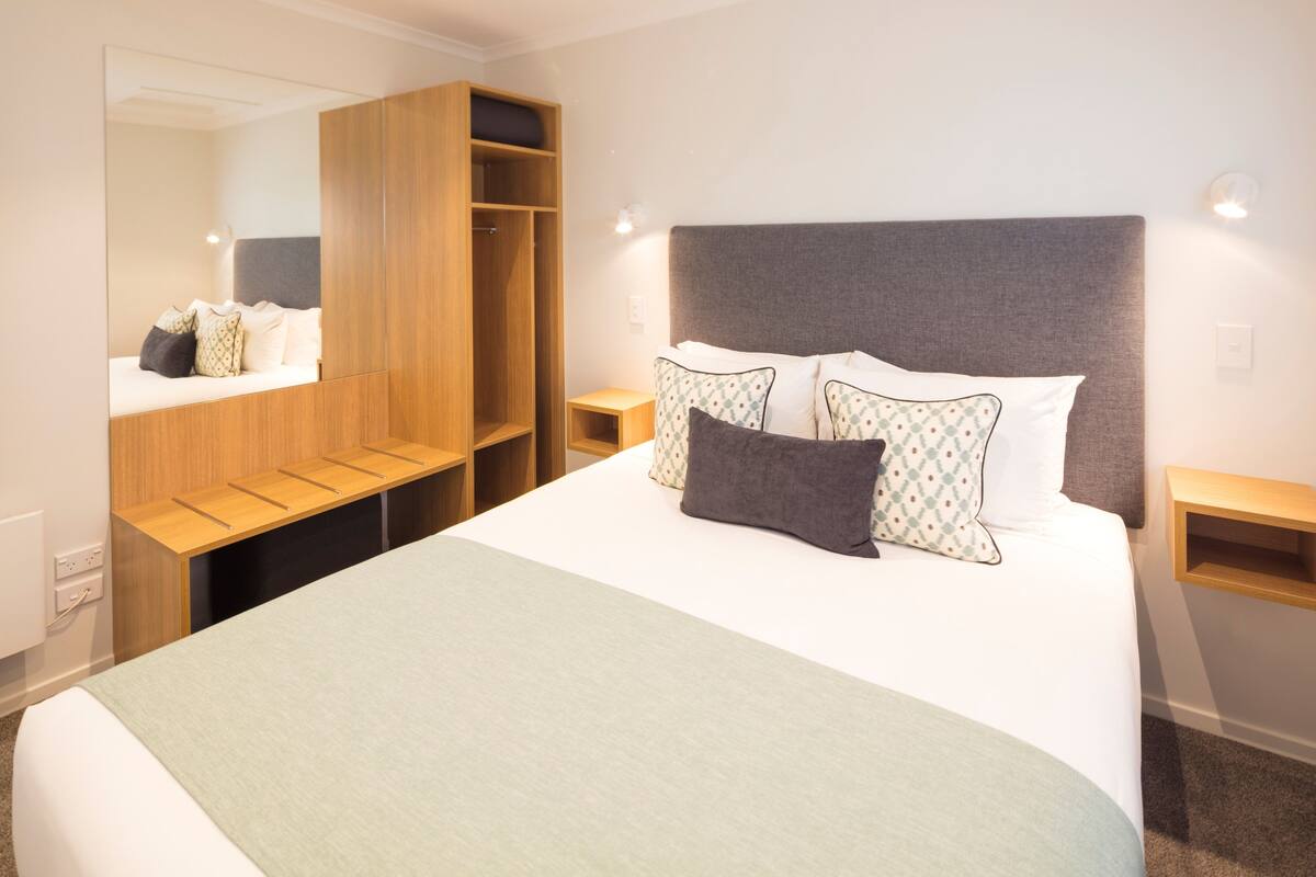 Un dormitorio ordenado con una cama grande, un armario y una mesita de noche.