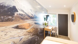 A room with a large mural of a mountainous landscape, a desk with a chair, a bed, and a door. - Beechwood Boutique Accommodation (Dunedin)