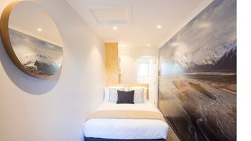 A hotel room with a large bed, a round mirror, a painting of a snowy landscape, and a wooden accent wall.