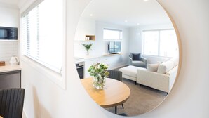 A modern living room with a round mirror reflecting the space, a sofa, a coffee table, and a TV. - Beechwood Boutique Accommodation (Dunedin)