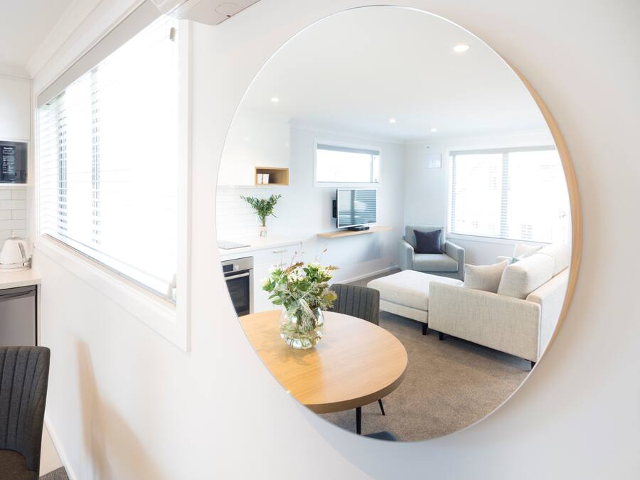A modern living room with a round mirror reflecting the space, a sofa, a coffee table, and a TV.
